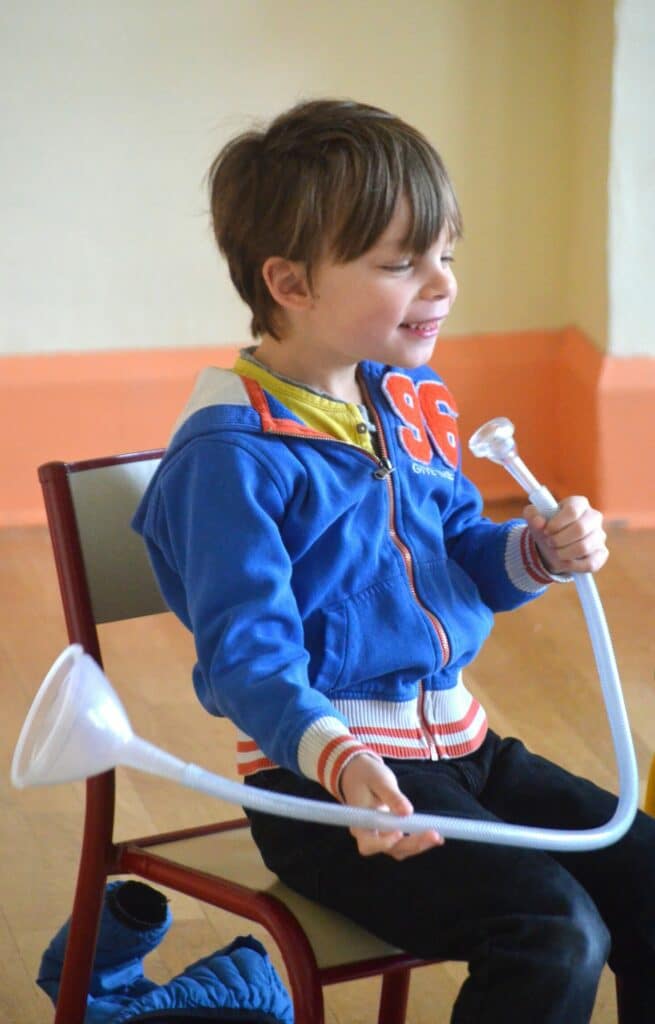 Jeune garçon qui joue avec un tube en plastique doté d'un entonnoir, représentant le système sonore des instruments à embouchure